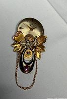 Front view of brooch showing watch dial, gears, charms and chain