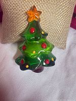 Front view of translucent green Christmas tree brooch with red and yellow accents and orange star