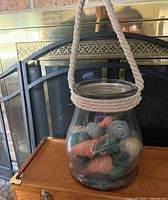 Full view of glass vase hanging by rope handle, filler visible