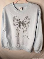 Front view of light blue crewneck sweatshirt with bow graphic and bead embellishments