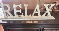 Front view of mint green wooden RELAX sign on dark furniture
