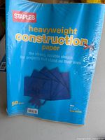 Front view of sealed Staples heavyweight construction paper pack displaying branding, sheet count and color