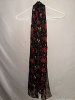 Full view of long black scarf with holiday print hanging on hanger