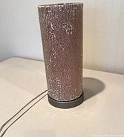 Full view of cylindrical table lamp showing pink crackle finish and metal base