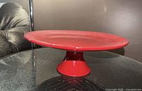 Side view of red ceramic pedestal cake stand on glass table