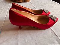 Side view showing red satin pump, kitten heel, rhinestone brooch