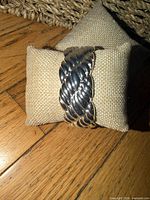 Front view of silver plated twisted rope hinged cuff bracelet on burlap pillow