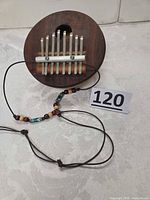 Full view of kalimba showing wood top, metal tines, lanyard and lot number