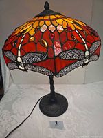 Front view of lamp illuminated showing stained glass dragonfly motif shade and metal base