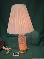 Full view of lamp illuminated with pleated shade, cord and base visible