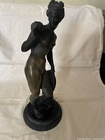 Front view of bronze female figure holding sphere, showing overall form and base