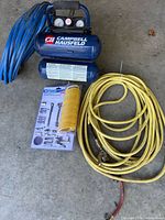 Overall lot showing blue twin-tank air compressor, blue hose, sealed coiled hose kit, and yellow hose