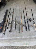 Group of eight fishing rods and one rod case laid out on floor