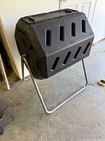 Overall view of black plastic rotating drum composter on metal stand