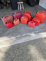 Group of nine red/orange plastic gasoline containers of various sizes lined on garage floor