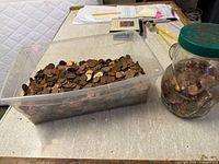 Plastic bin and glass jar partially filled with pennies on tabletop