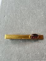 Front view of gold-filled tie clip showing enamel logo and red stones