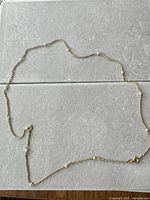 Full view of gold-tone station necklace laid flat showing length and clasp