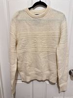 Full view of ivory wool sweater on hanger showing overall design