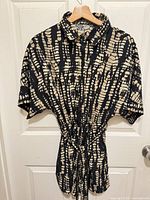 Front view of black and beige tie-dye romper hanging on hanger