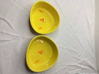 Pair of yellow ceramic chick treat dishes displayed top and bottom on white surface