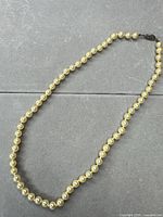 Full view of cream faux pearl necklace showing gold-tone accents and clasp