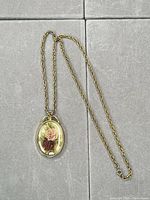 Full view of gold-tone necklace and oval floral pendant