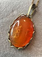 Oval amber-orange cabochon pendant in scalloped gold-tone bezel on chain