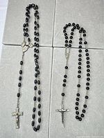 Both black plastic rosaries laid out showing bead styles, crucifixes and medals