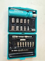 Open Makita teal case showing driver handle, sockets, bits and accessories