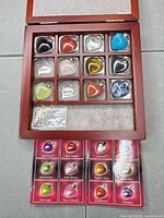 Display box open showing gemstone pendants in 12 slots with identification card and chain in bag