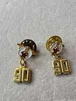 Front view of both identical gold-tone crescent and star lapel pins with dangling "90" charms and butterfly clutches