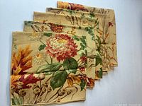 Four folded beige napkins with multicolor autumn floral design displayed on white surface