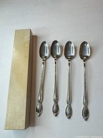 Four long ornate silver-plated spoons beside a narrow box