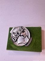 Front view of silver-tone "BROKE" money clip on green base