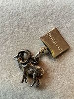 Close-up of silver-tone ram charm, attached jump ring and square tag visible