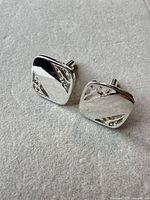 Front view of both cufflinks showing square faces, engraved details, and bullet backs