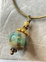 Close-up of iridescent green lampwork glass bead pendant with gold-tone accents on snake chain necklace