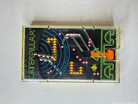 Front view of Tomy Catch A Caterpillar pocket game showing playfield, balls, and launcher