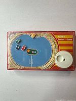 Front view of red Tomy Speedway pocket game showing racetrack graphic, built-in winder and four race car pieces