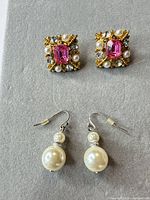 Both pairs of earrings displayed on fabric background: square jeweled clip-ons above, pearl drop fishhooks below