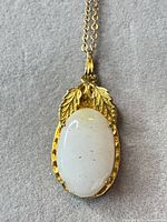 Front view of gold-tone leaf pendant necklace with white cabochon
