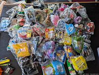 Large pile of 70+ sealed McDonald’s Happy Meal toys of various franchises spread on table