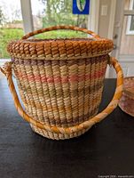 Side view of round woven basket with lid and twisted handle