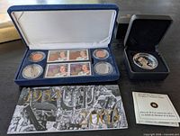 Open blue case showing six coins, four stamps, adjacent black coin case and booklet