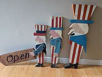 Three carved wooden Uncle Sam figures, one holding an “Open” sign