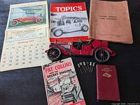 All items laid out: five publications, calendar, cast iron car, six pins