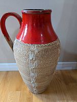 Full front view showing red glazed neck, single handle, textured lava body