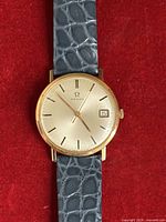 Front view of Omega 18k gold watch on grey leather strap showing dial and hands