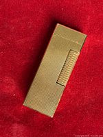 Front view of gold-tone textured lighter showing roller and hinged lid